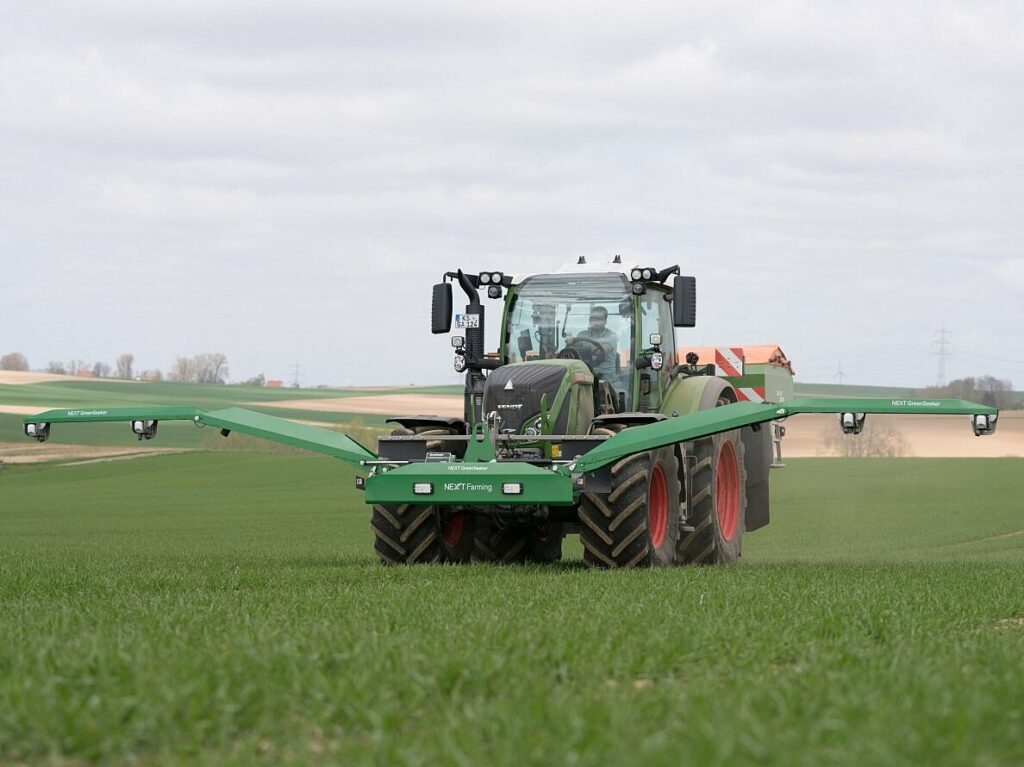 Ein Traktor düngt eine Wiese mit einem Düngerstreuer und den NEXT Farming Green Seeker.